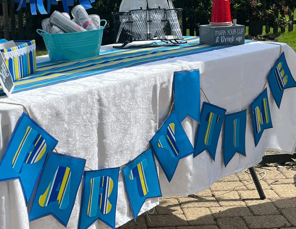 4 - C'mon Get Crafty closeup of blue outdoor fabric pennant banner on front of white linen covered table with table runner and outdoor party decor.