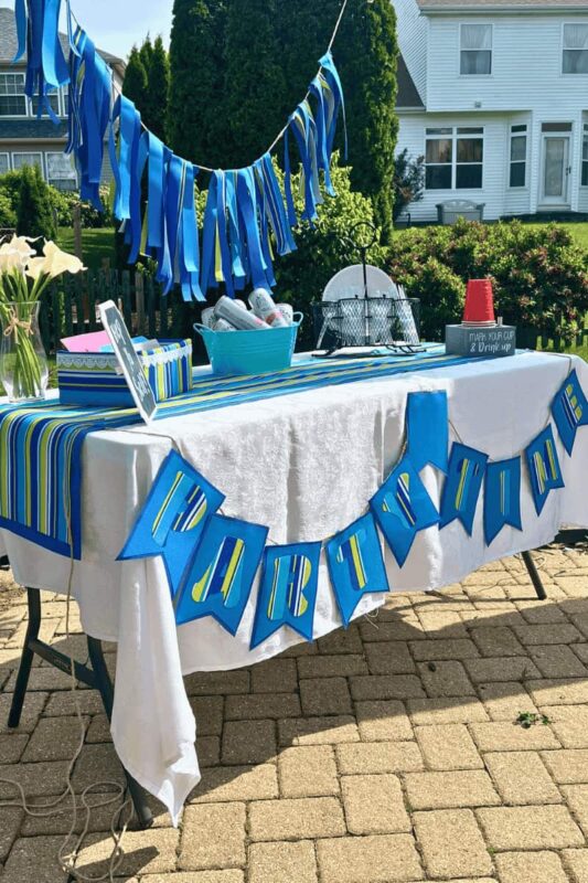 Outdoor Fabric table set up no backdrop OPT - C'mon Get Crafty closeup of blue outdoor fabric pennant banner on front of white linen covered table with table runner and outdoor party decor.