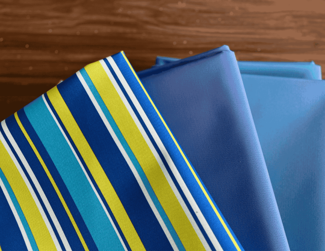Untitled design - C'mon Get Crafty blue, white, and green striped canvas fabric bolts on wooden surface