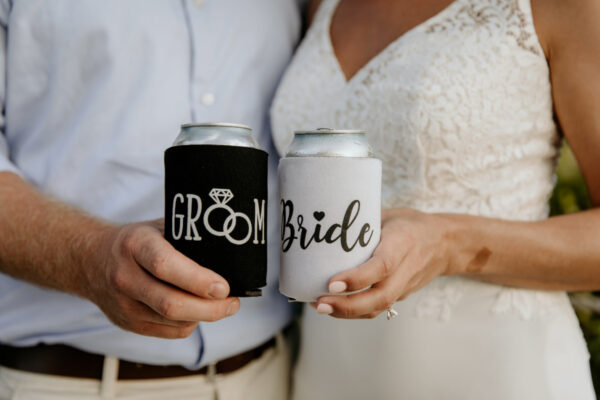 Bride and Groom Koozies - C'mon Get Crafty A man and woman are holding cans in can coolers. The man’s cooler is black and says "Groom" with a diamond graphic. The woman’s is white and says "Bride" in black cursive.