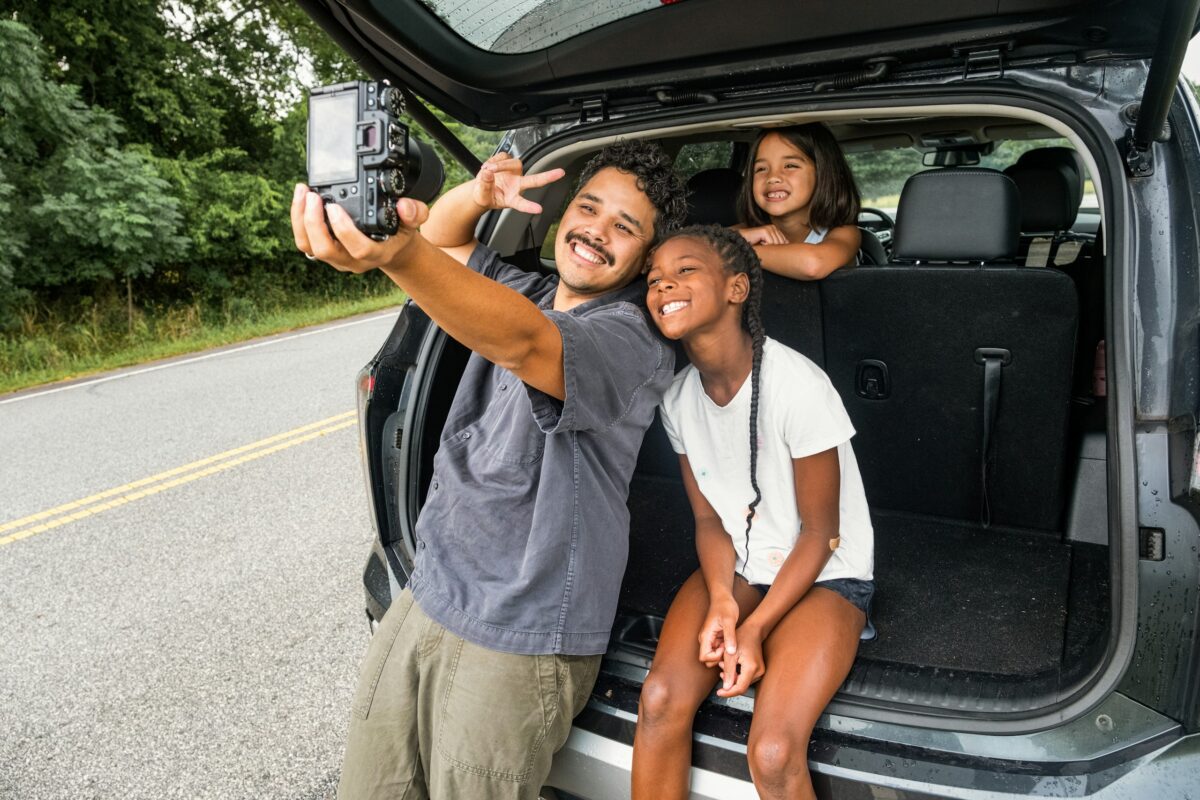 father-and-daughters-take-a-selfie-by-the-car-stockpack-unsplash - C'mon Get Crafty man and female child taking a selfie in the back of a car on a road trip